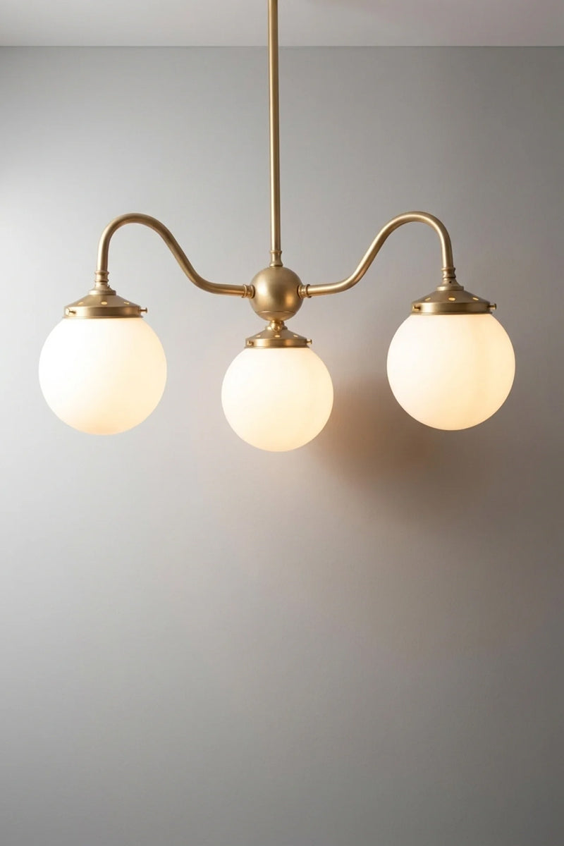 small gold three light pendant with opal glass globes on curved arms, lit against a plain grey backdrop