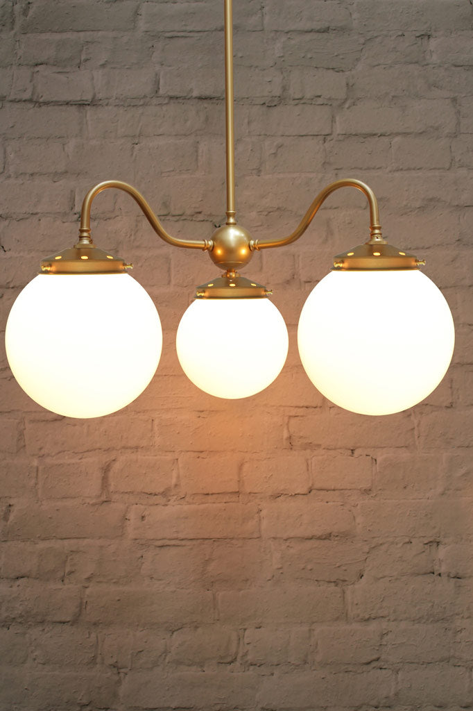 Large, opal glass ball shades on a triple gold/brass gooseneck chandelier fixture. 