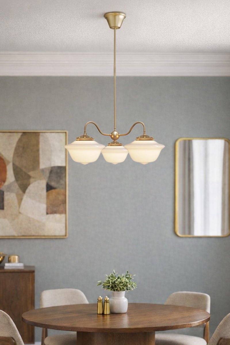 Gold/brass three arm gooseneck changalier with schoolhouse shades over a dining space. 