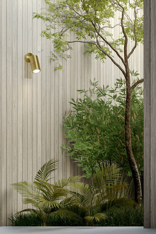 Polished brass adjustable wall light on light timber panelling in a courtyard. 
