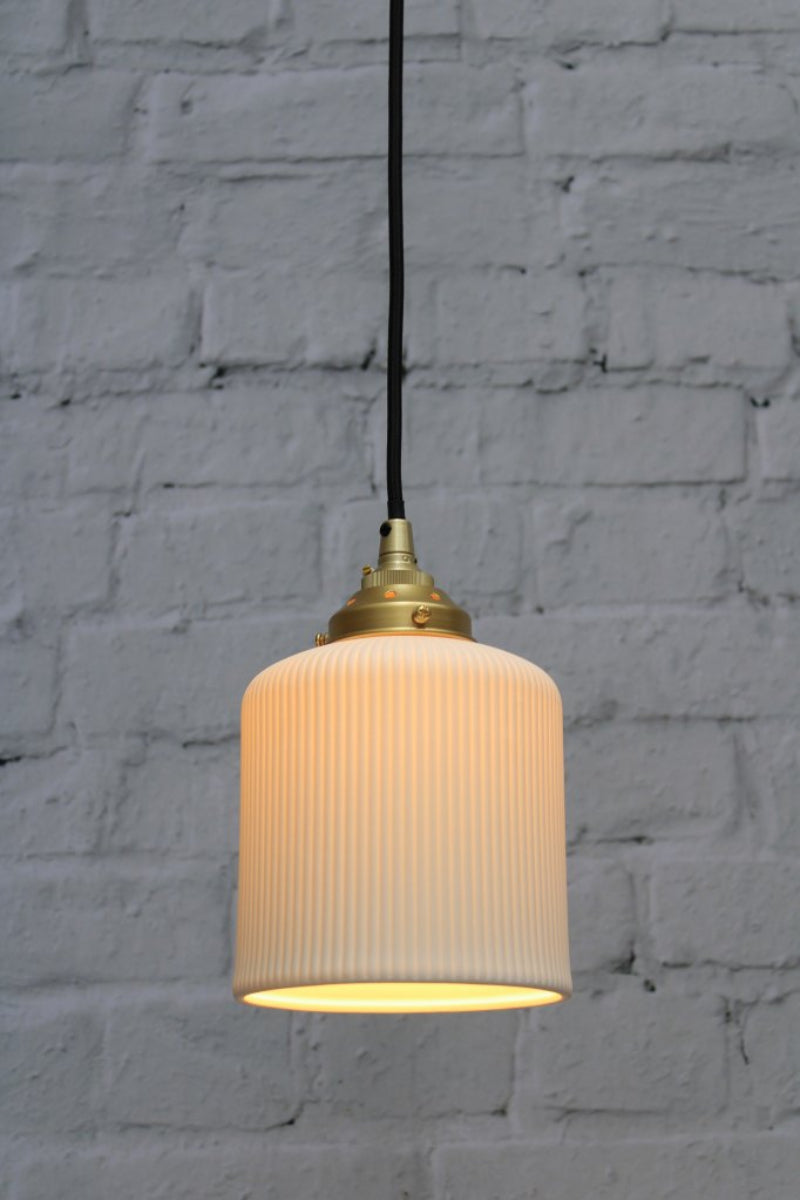 Ribbed ceramic pendant light with black cord and gold/brass hardware.