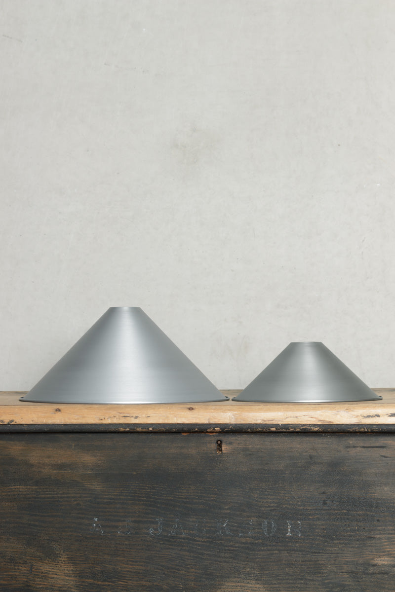 Small and large vintage steel cone shades placed on a timber bench. 