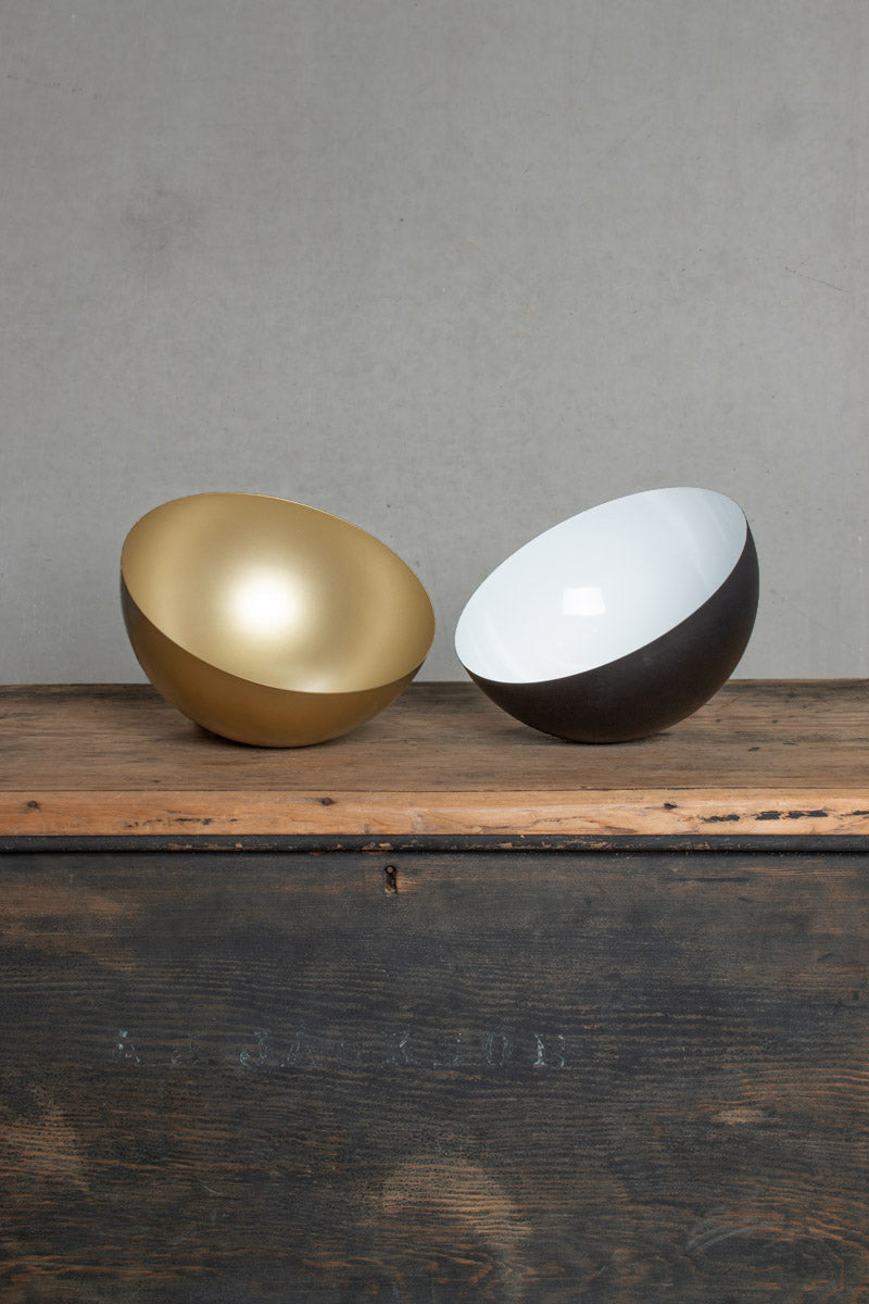 Matt black and brushed brass dome pendant light shade finishes displayed side by side on a rustic timber surface.