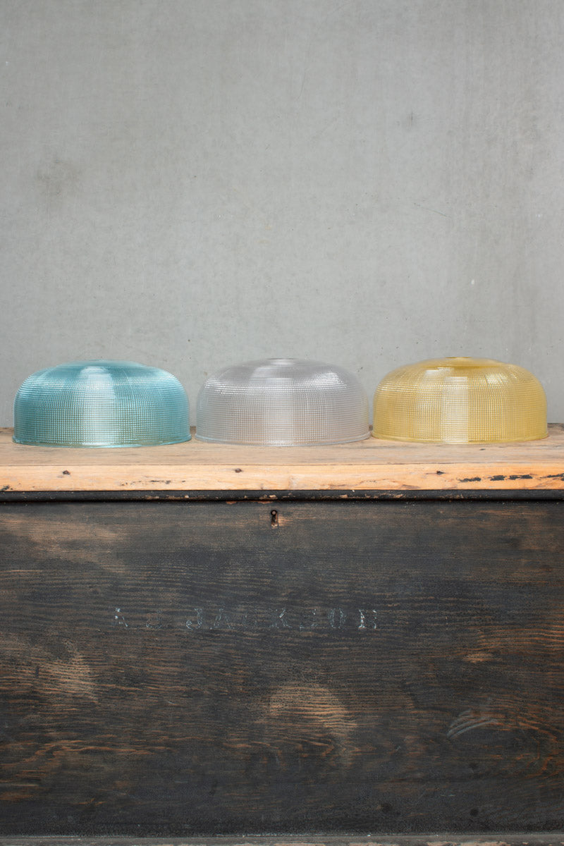 Three large holophane style glass shades in blue, clear and amber, sitting on a timber bench. 