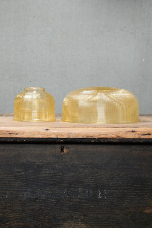 Small and large amber holophane style glass shades on a timber bench. 