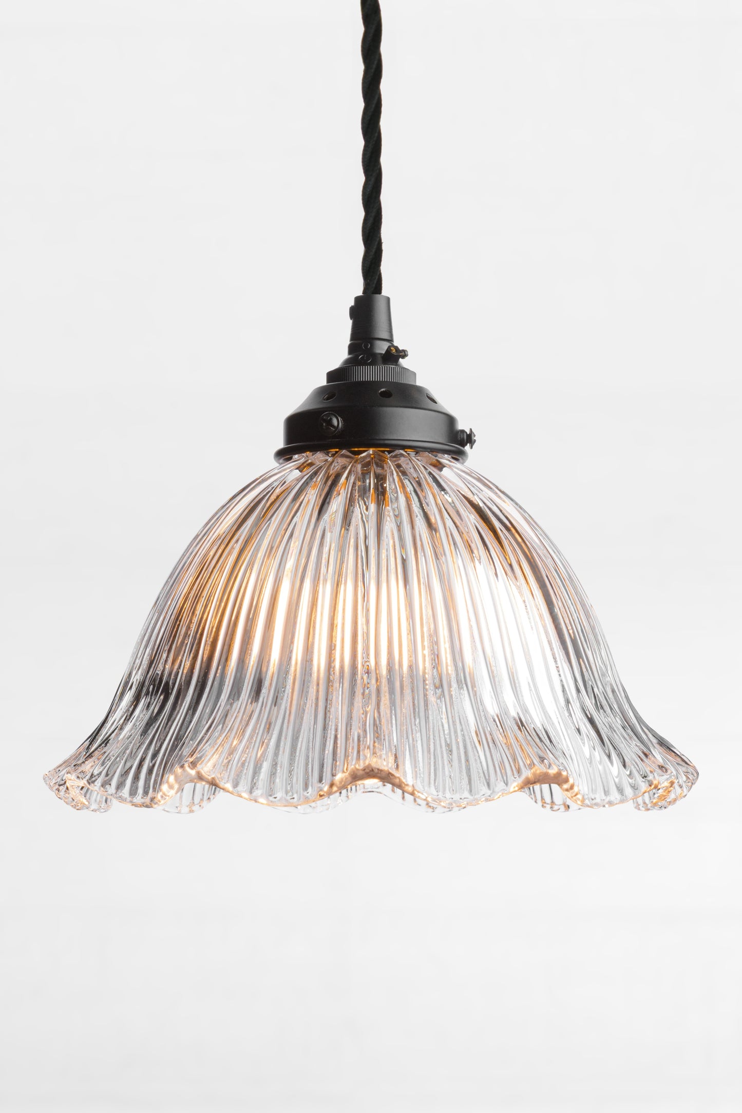 Black tisted cloth cord, black lampholder and gallery paired with a large clear glass shade with frilled edge and ribbed detailing. 
