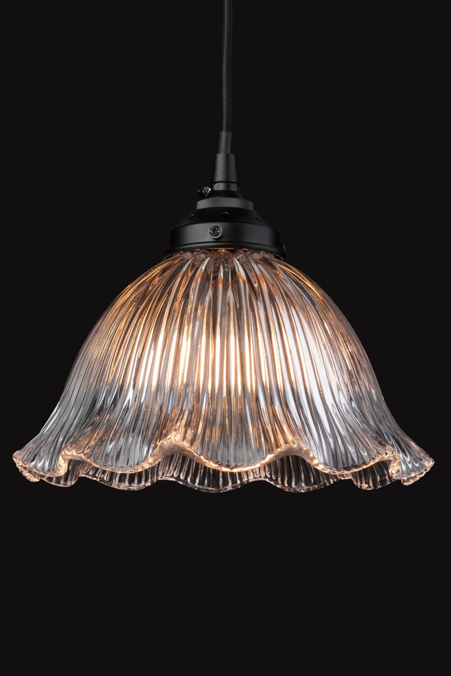 Frill edged clear shade with ribbed detailing and black cord in a black room rocasing the ineresting light distribution. 