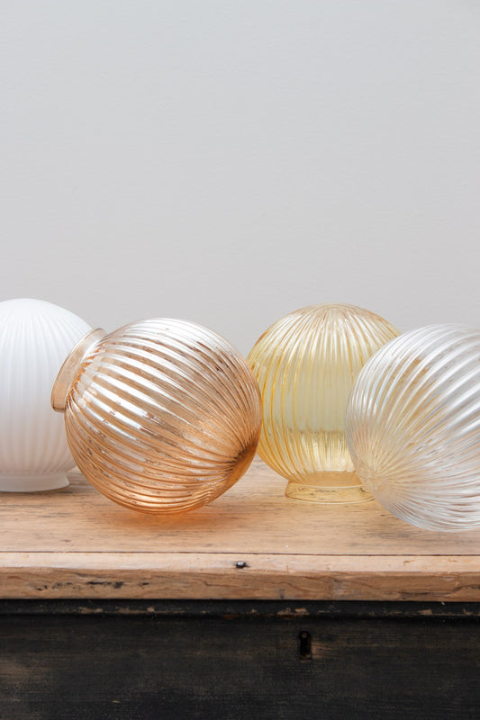 Glass ball shades in dark amber, opal, clear and amber finishes with reeded detailing on a timber bench. 