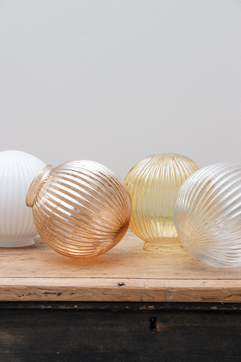 Glass ball shades in dark amber, opal, clear and amber finishes with reeded detailing on a timber bench. 