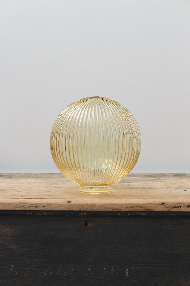 Medium amber reeded glass Dakota shade, placed on a timber bench against a light grey wall. 