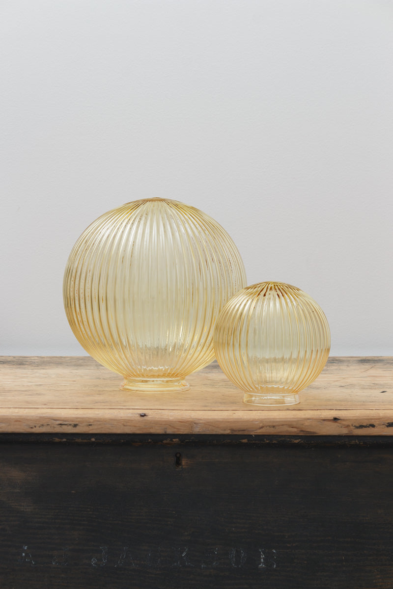 Medium and small amber reeded glass ball shades, placed on a timber bench. 