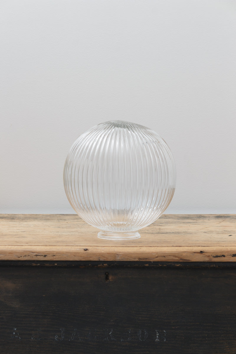 Medium clear reeded glass Dakota shade, placed on a timber bench against a light grey wall. 