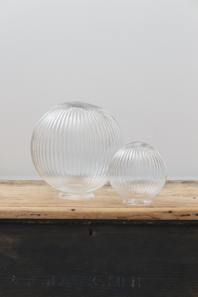 Medium and small clear reeded glass ball shades, placed on a timber bench. 