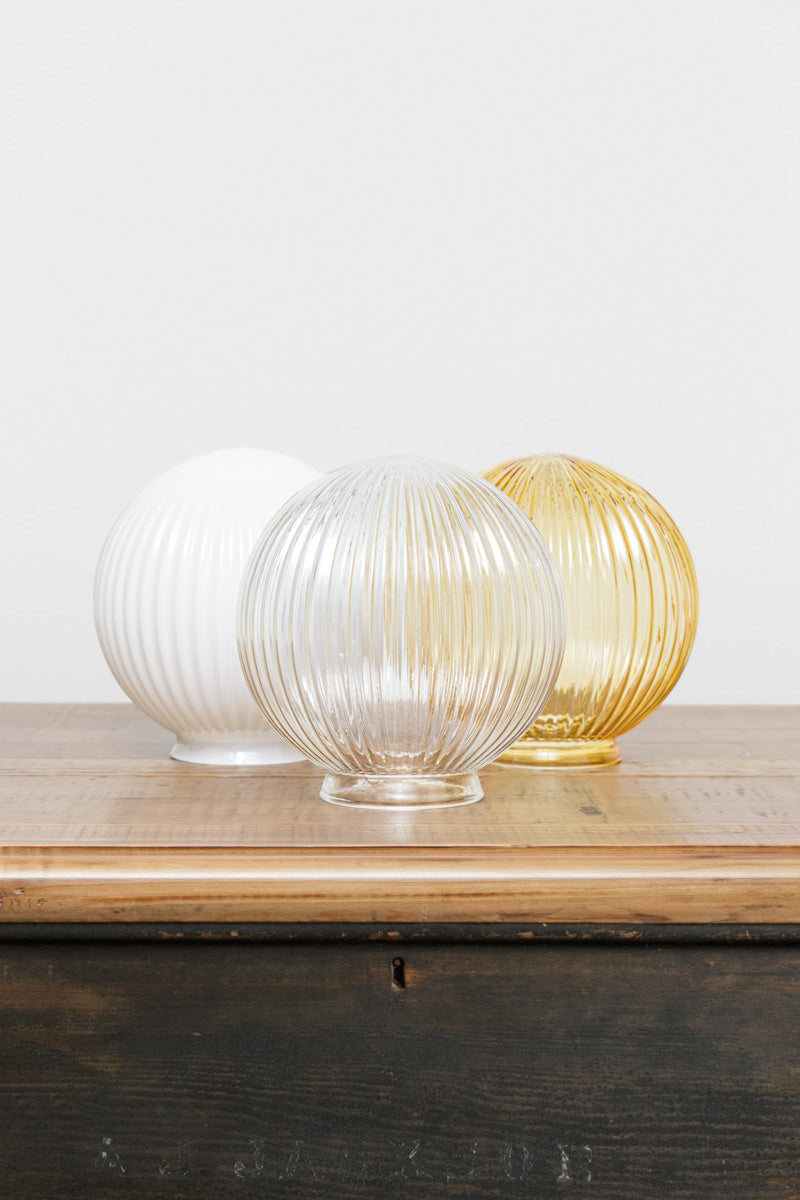 Glass ball shades in opal, clear and amber finishes with reeded detailing on a timber bench. 