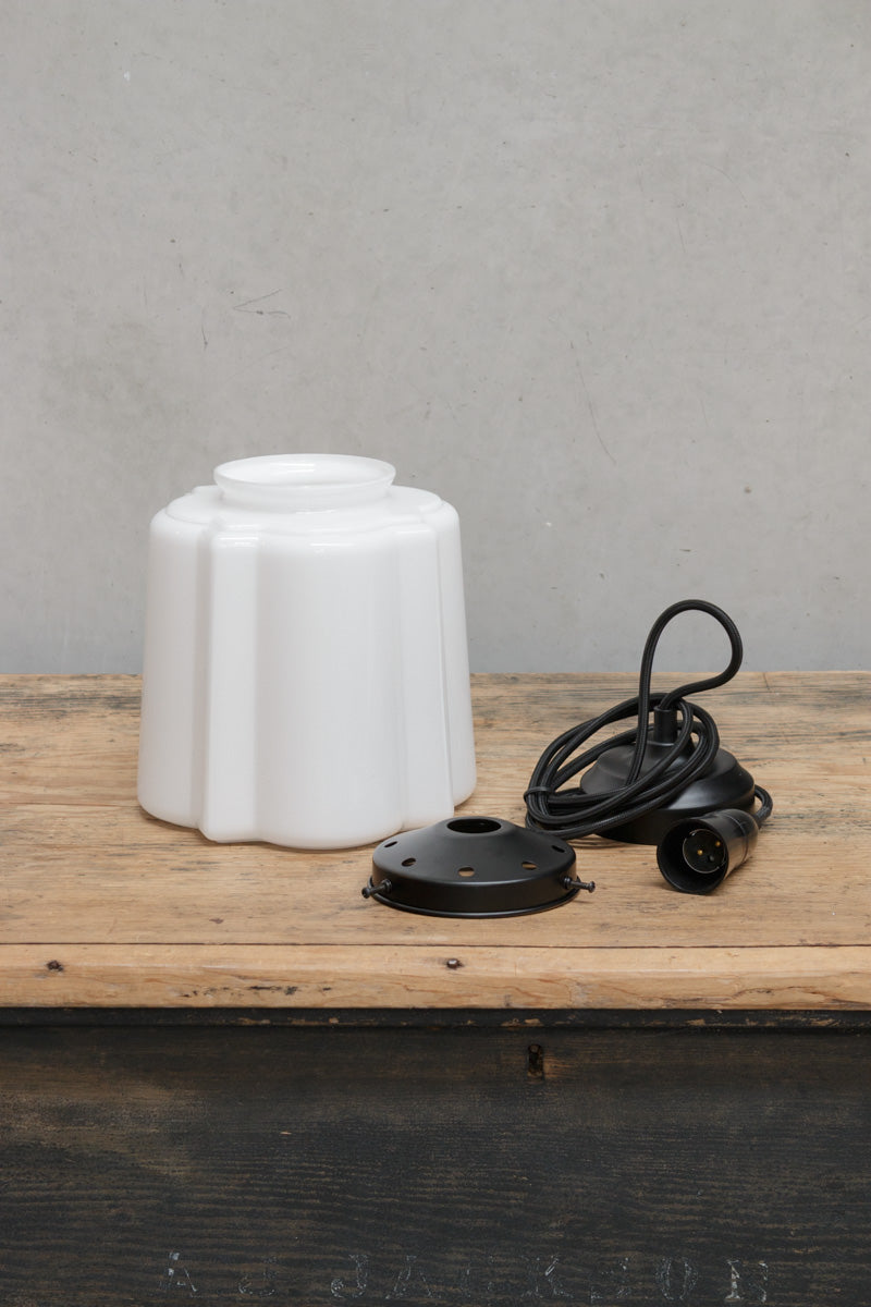 Uninstalled deco glass shade with a flat bottom, set out with a black pendant cord and hardware. 