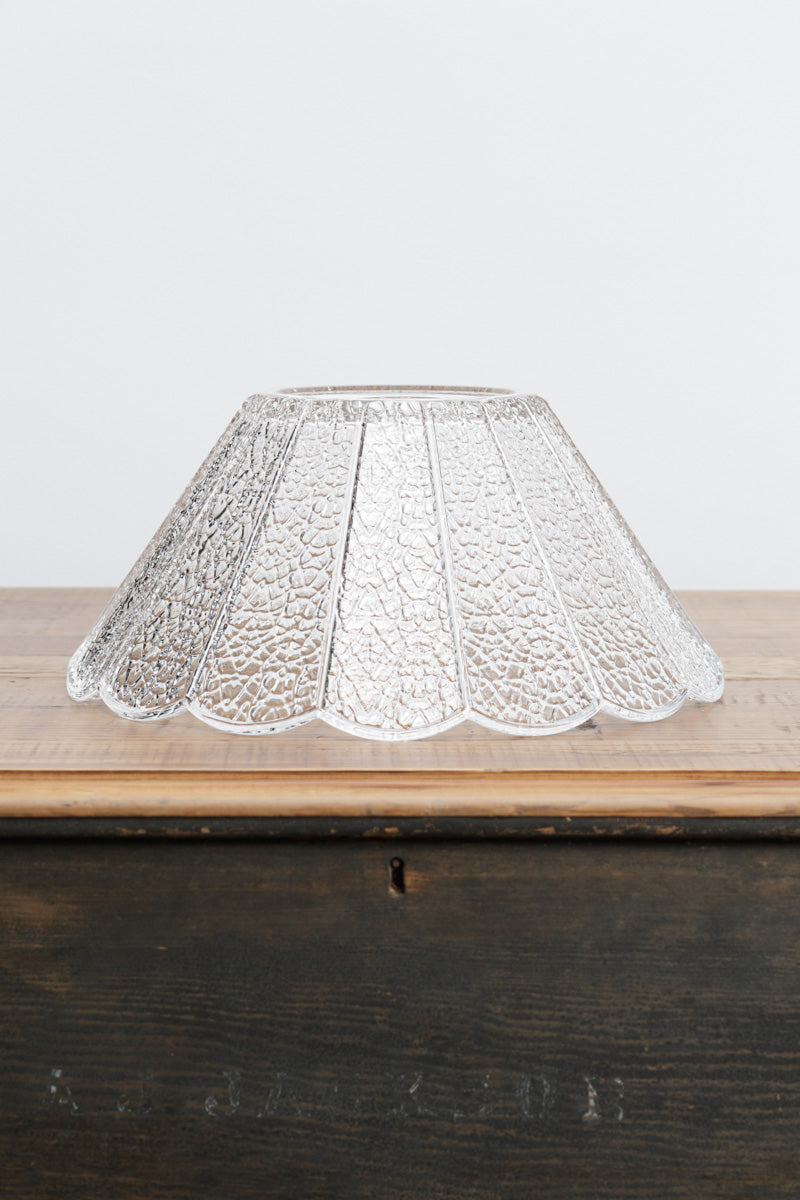 Uninstalled clear crackle glass shade with scalloped edge, sitting on a timber bench. 
