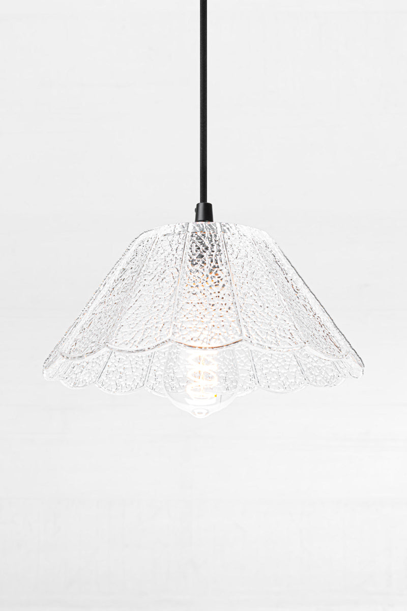 Clear crackle glass shade with scalloped edge on a black cloth pendant cord, paired with a teardrop bulb. 