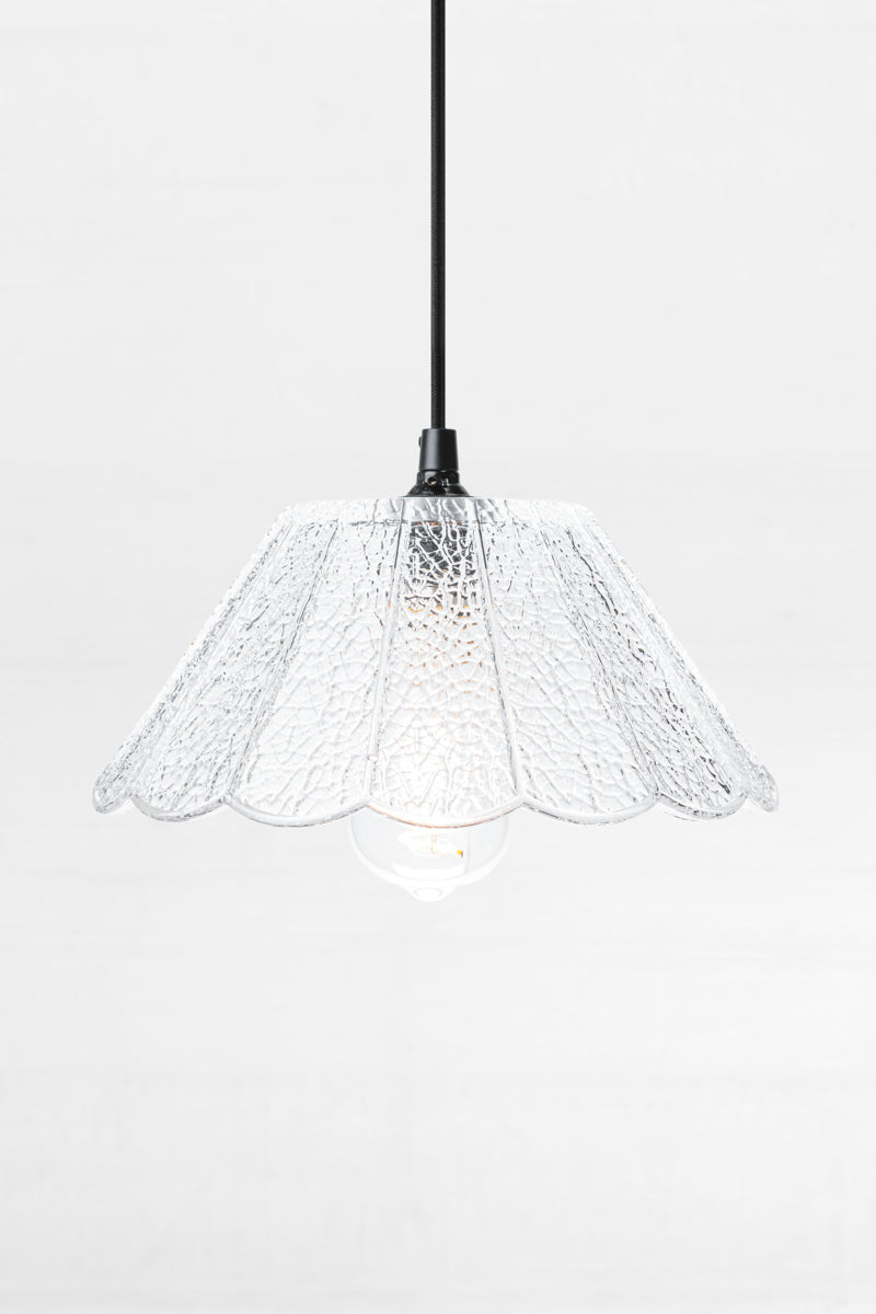 Clear crackle glass shade with scalloped edge and flat top, on a black cloth pendant cord. 