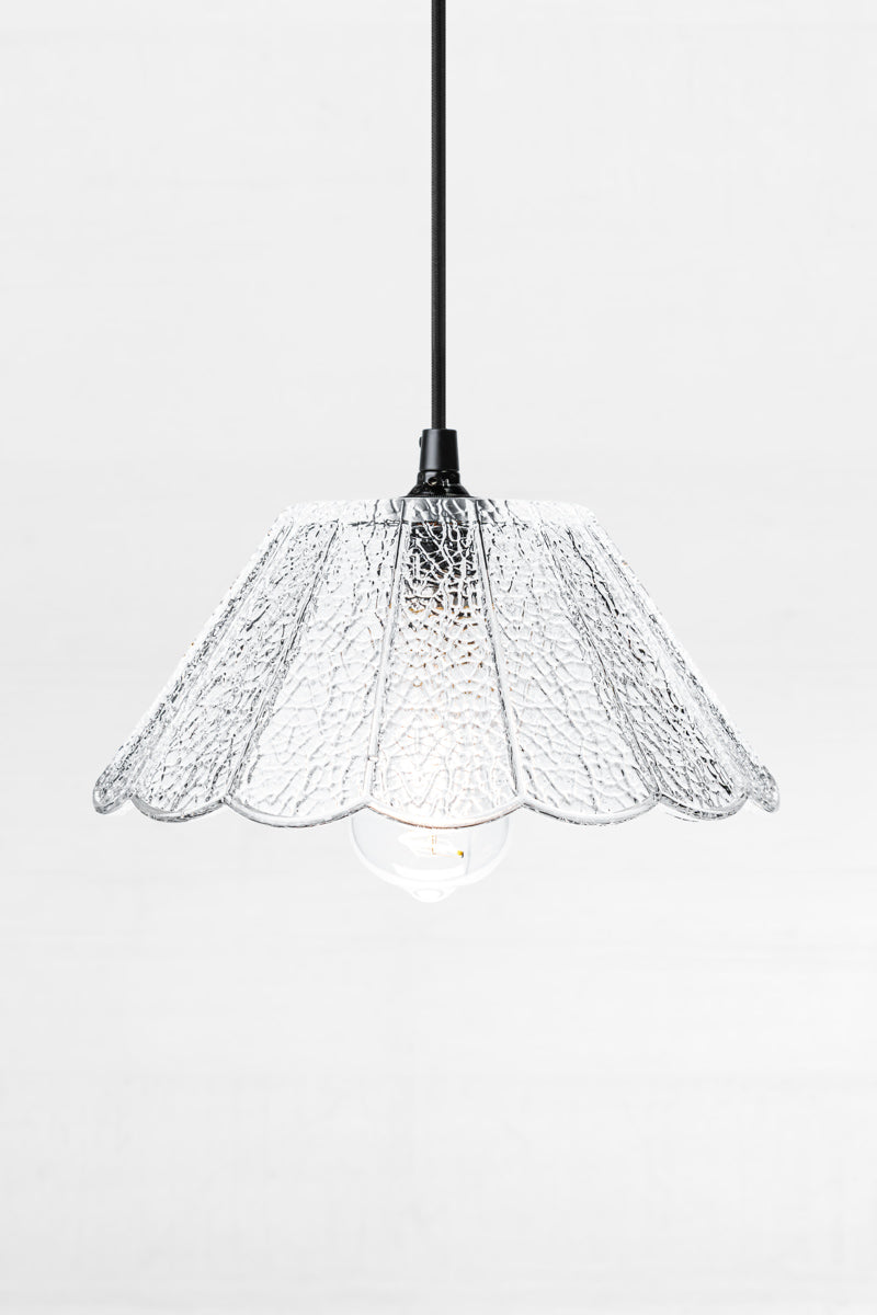 Clear crackle glass shade with scalloped edge and flat top, on a black cloth pendant cord. 