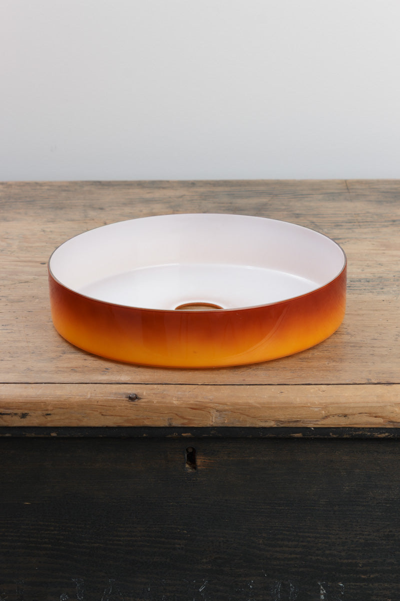 Amber circular shade with white inner, placed on a timber bench. 