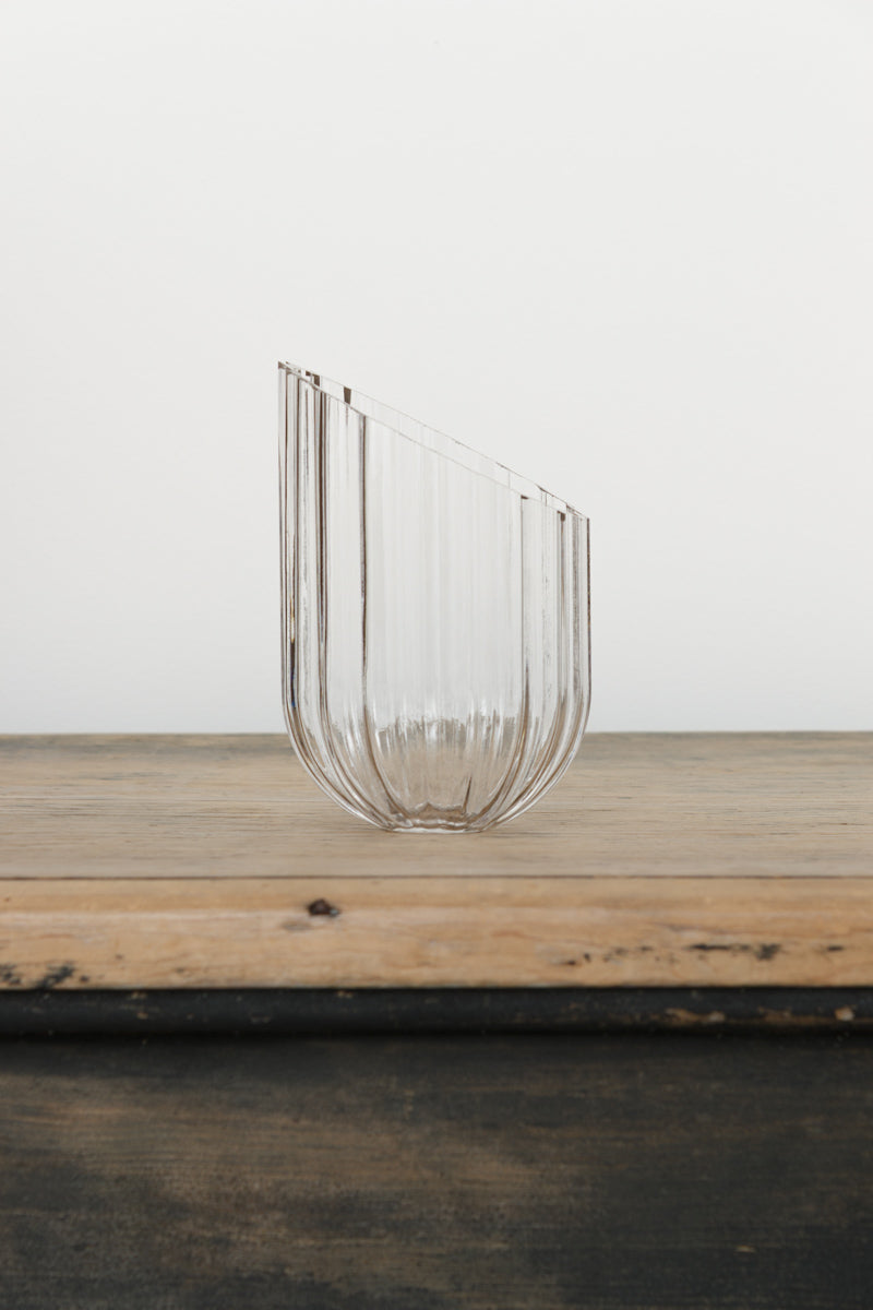 A clear glass shade with an elongated design, it has fluted detailing and features an angled cut edge. 