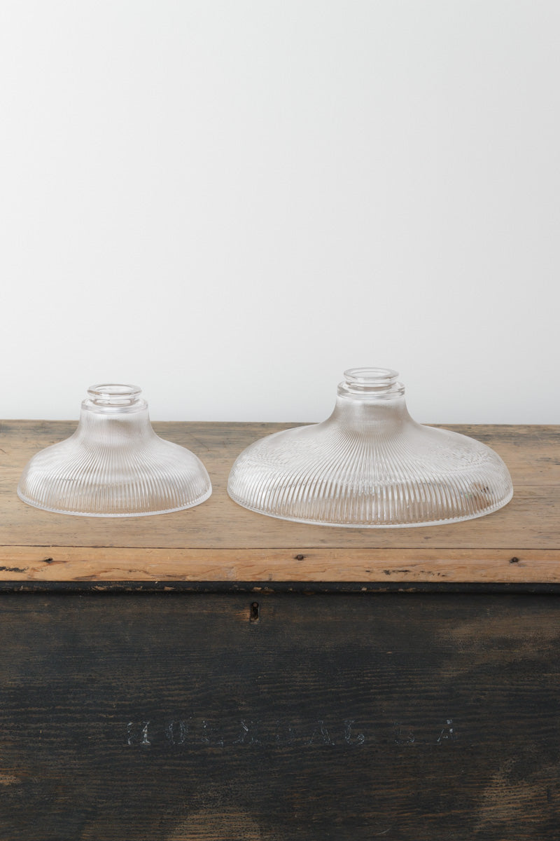 Large and small holophane pressed glass shades on a timber bench. 
