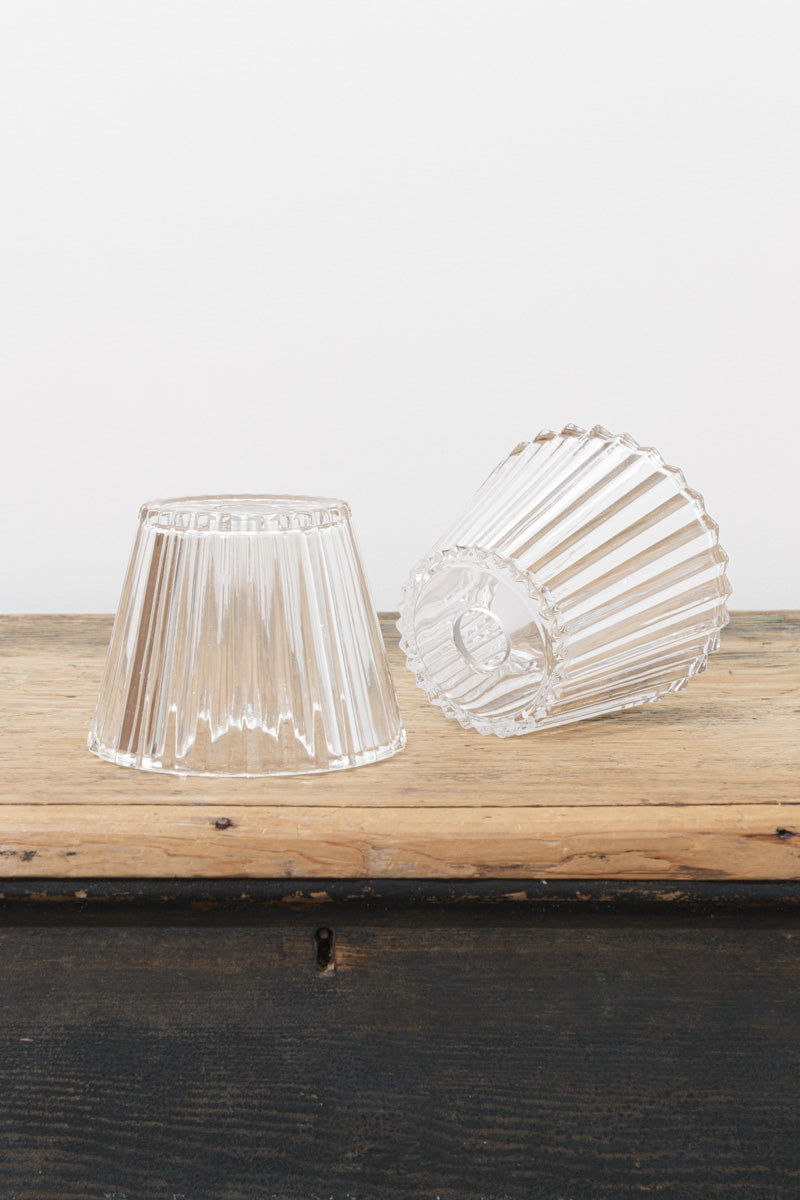 Clear fluted glass shades displayed on a rustic timber surface, showcasing the tapered silhouette and vertical ribbed detailing.
