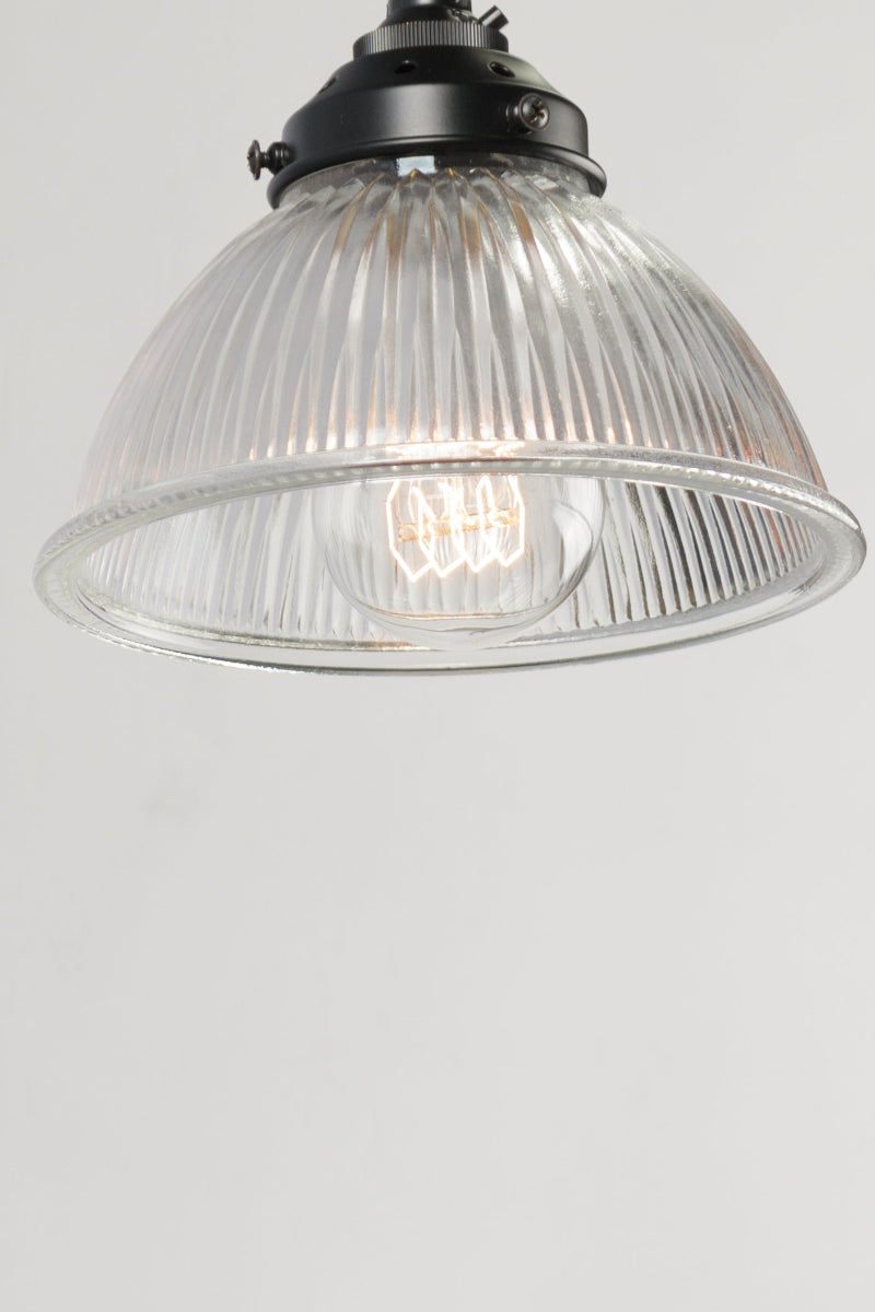trapeze cord light fixture with a clear glass shade on a white wall.
