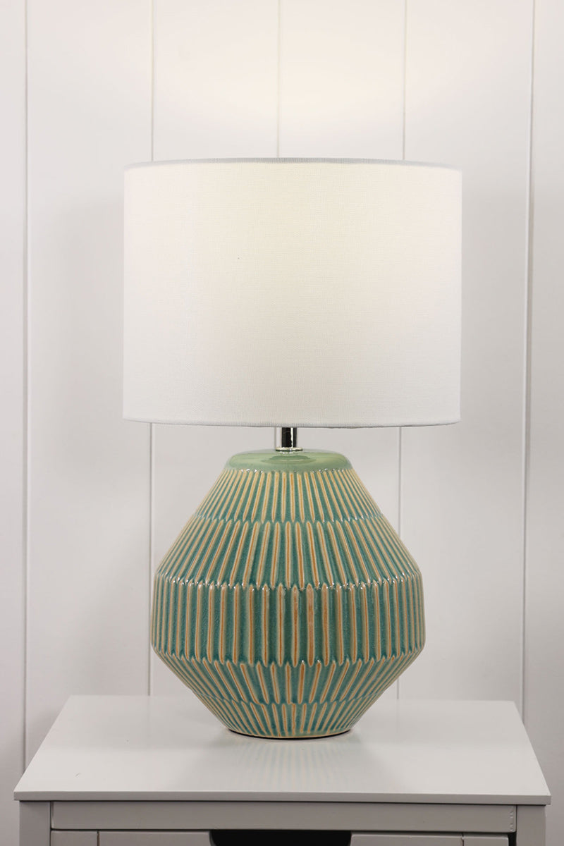 Green textured ceramic based table lamp with a white fabric shade on  side table. 