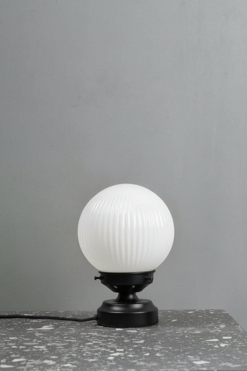 Reeded opal glass ball shade on a short black lamp stand. 
