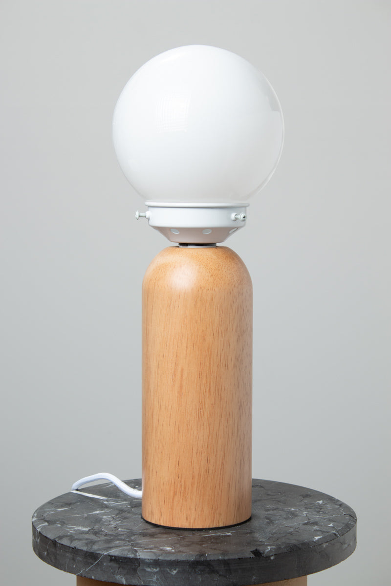 Opal glass ball shade, white gallery paired with a wood table lamp base on a marble look ride able, with the light turned off. 