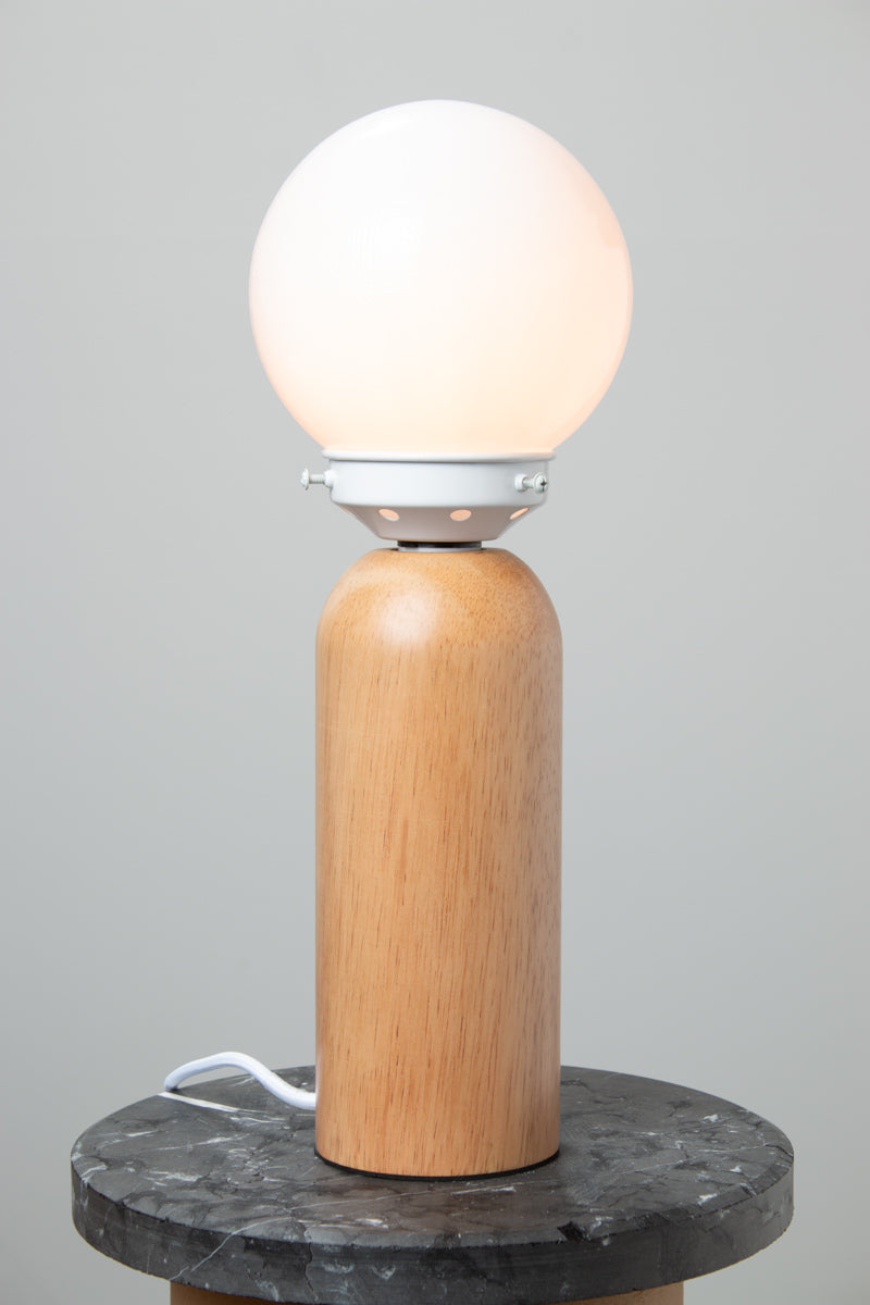 Opal glass ball shade, white gallery paired with a wood table lamp base on a marble look ride able, with the light turned on. 