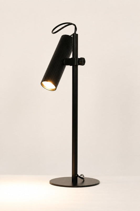 Black Collie desk lamp with the light on in a white space. 