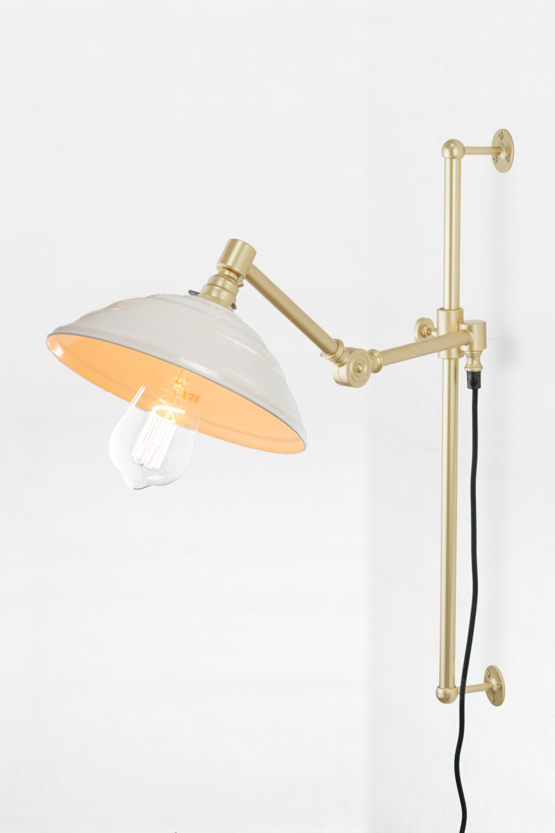 Swing Arm Wall Lamp in gold/brass arm finish with white Bakelite shade, paired with clear tear drop bulb. 