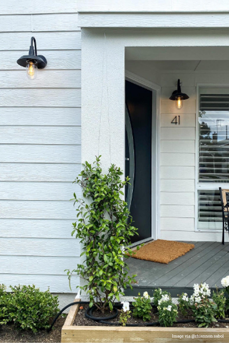Image via @rhiannon.sabol: Two gooseneck outdoor wall lights withe shades ang glass covers on the facade of a white weather baord house. 