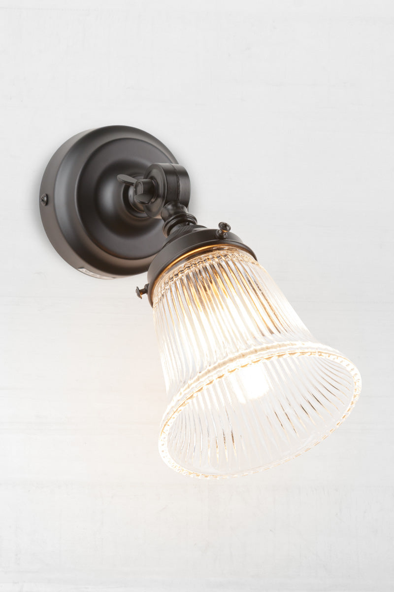 Slightly extended adjustable wall batten in black with a small clear glass shade with ribbed detailing.