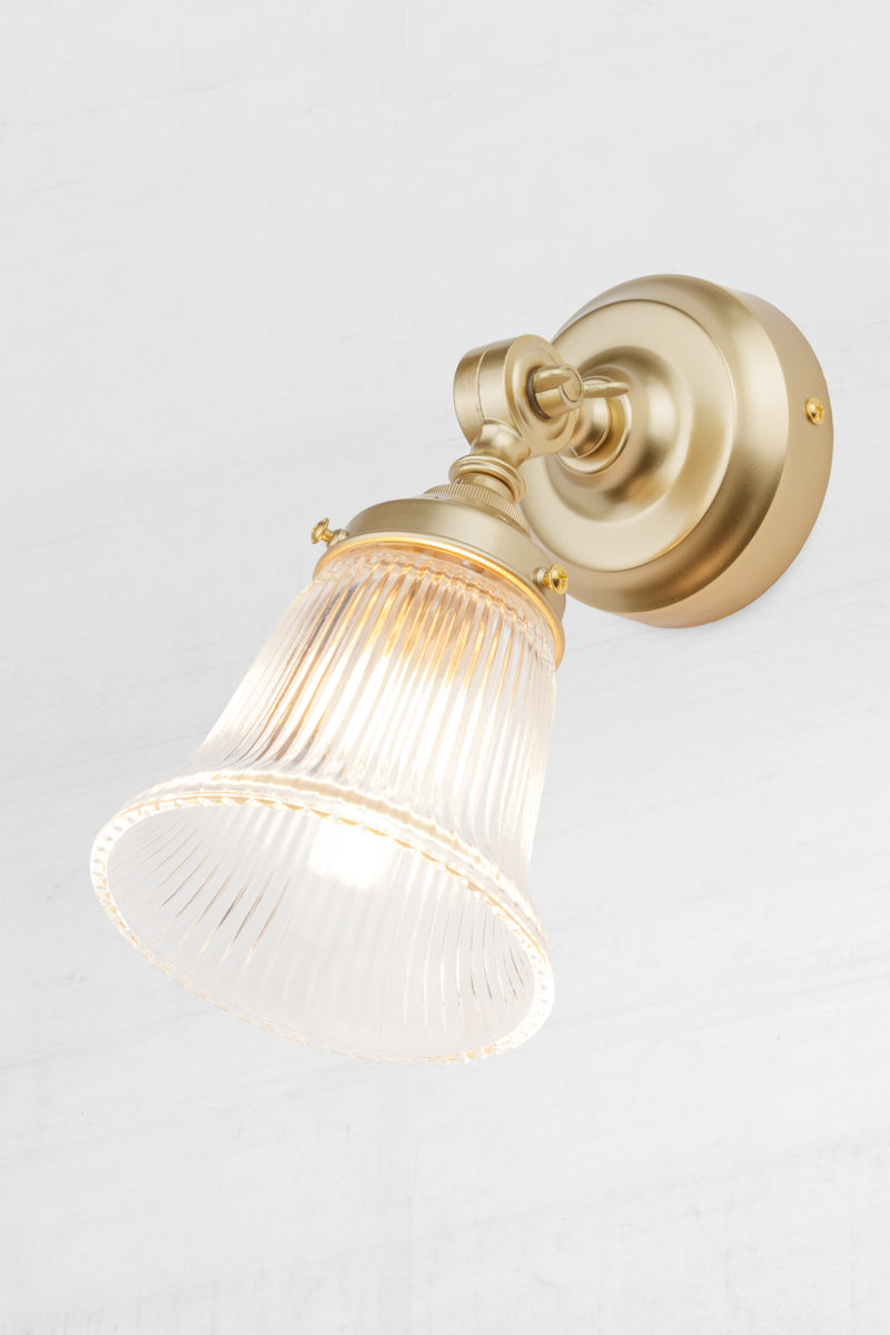 Slightly extended adjustable wall batten in gold/brass with a small clear glass shade with ribbed detailing.