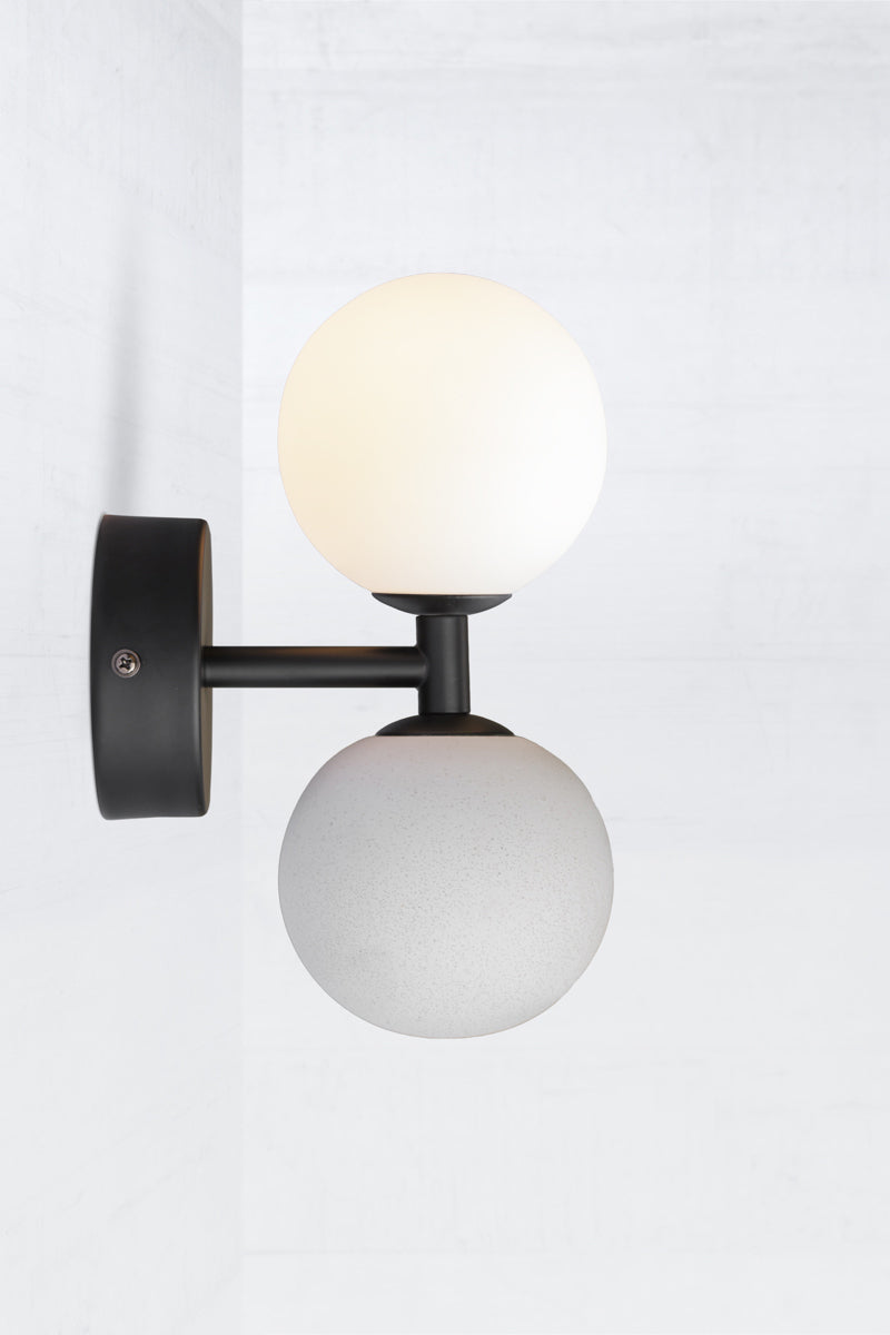 Side view of a modern wall sconce with black metalware opal glass ball shade and concrete ball feature.