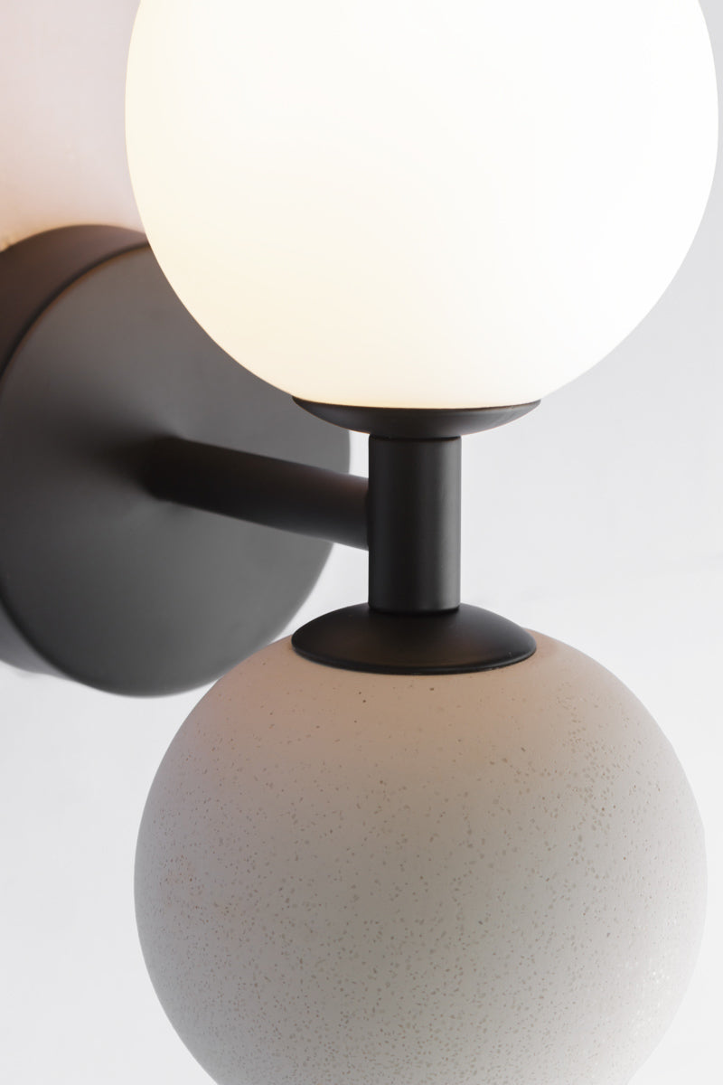 Close up of a modern wall sconce with black metalware opal glass ball shade and concrete ball feature.
