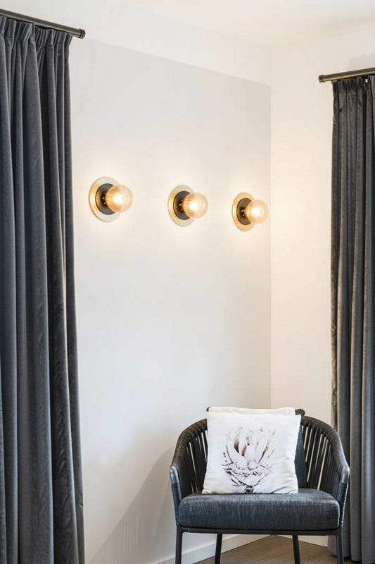 One amber reeded clear glass ball light with a small black disc and a large brass disc detail installed in a reading nook. 