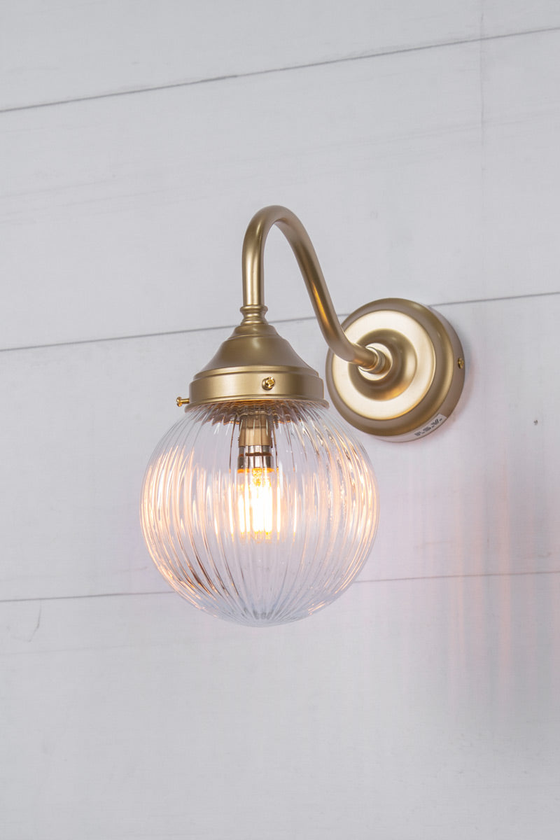 Exterior wall light with a gold gooseneck arm and clear reeded shade, side view.