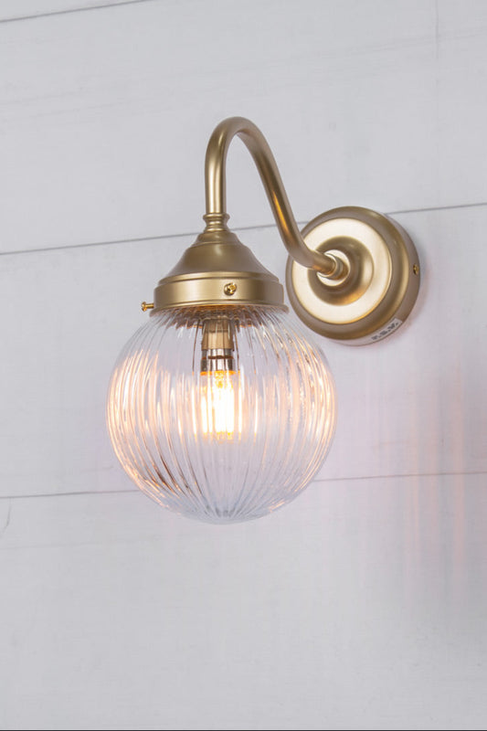 Exterior wall light with a gold gooseneck arm and clear reeded shade, side view.