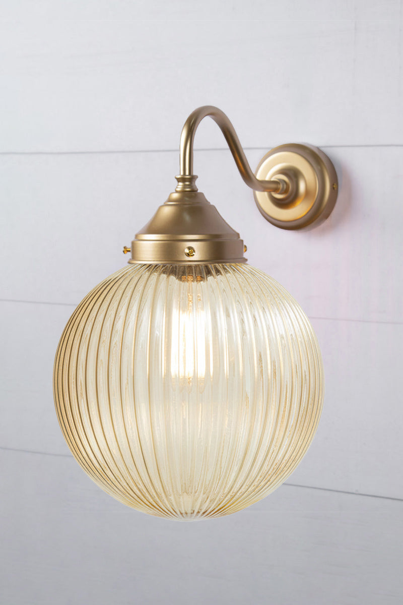 Exterior wall light with a gold/brass gooseneck arm and a medium amber reeded shade, side view.