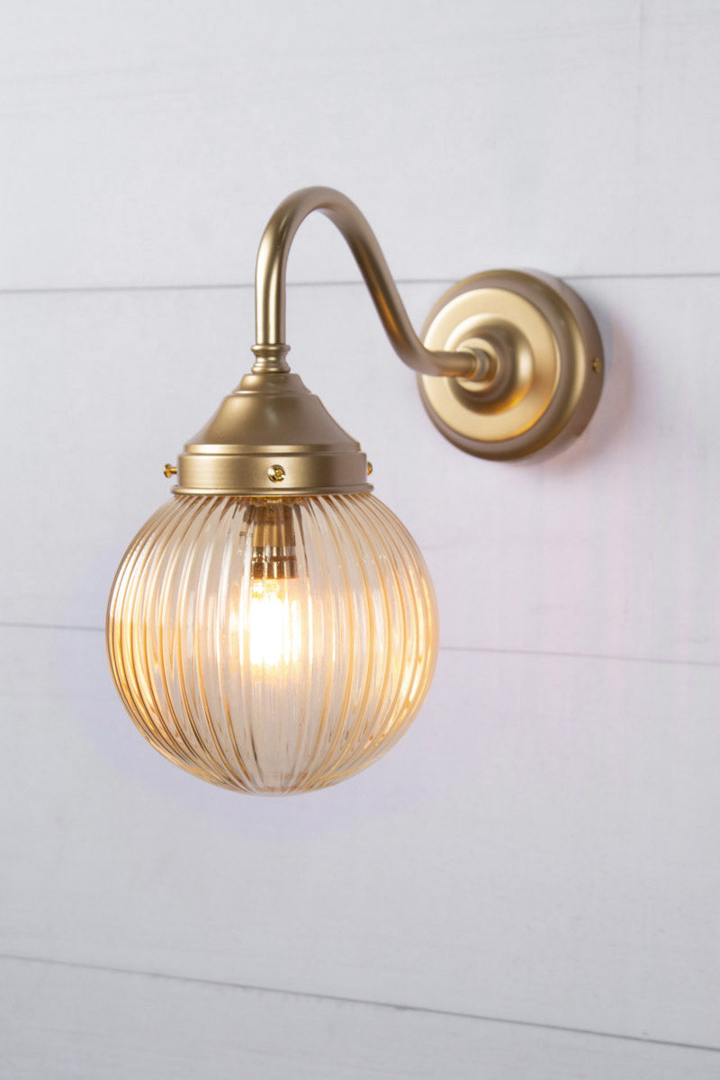 Exterior wall light with a gold/brass gooseneck arm and amber reeded shade.