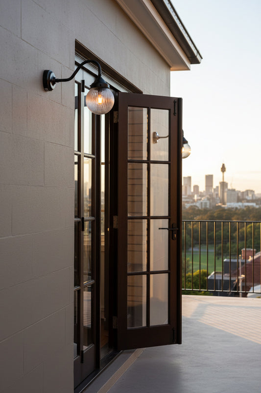 Two black gooseneck wall sconce lights with clear reeded glass ball shades either side of timber french doors. 
