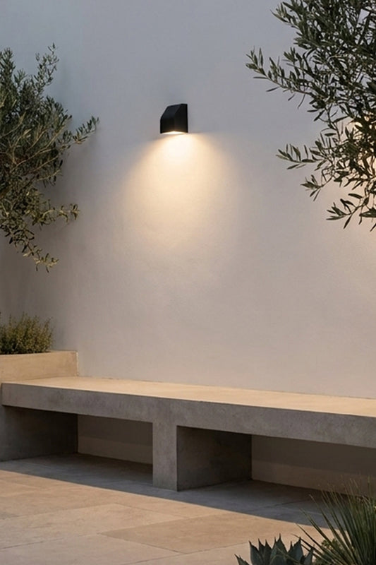 Matt black wall light over a modern concrete style bench seat with Mediterranean greenery.