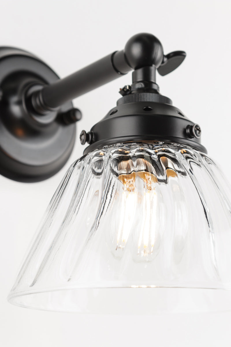 Close up of the short straight wall sconce in black with a clear shade. 