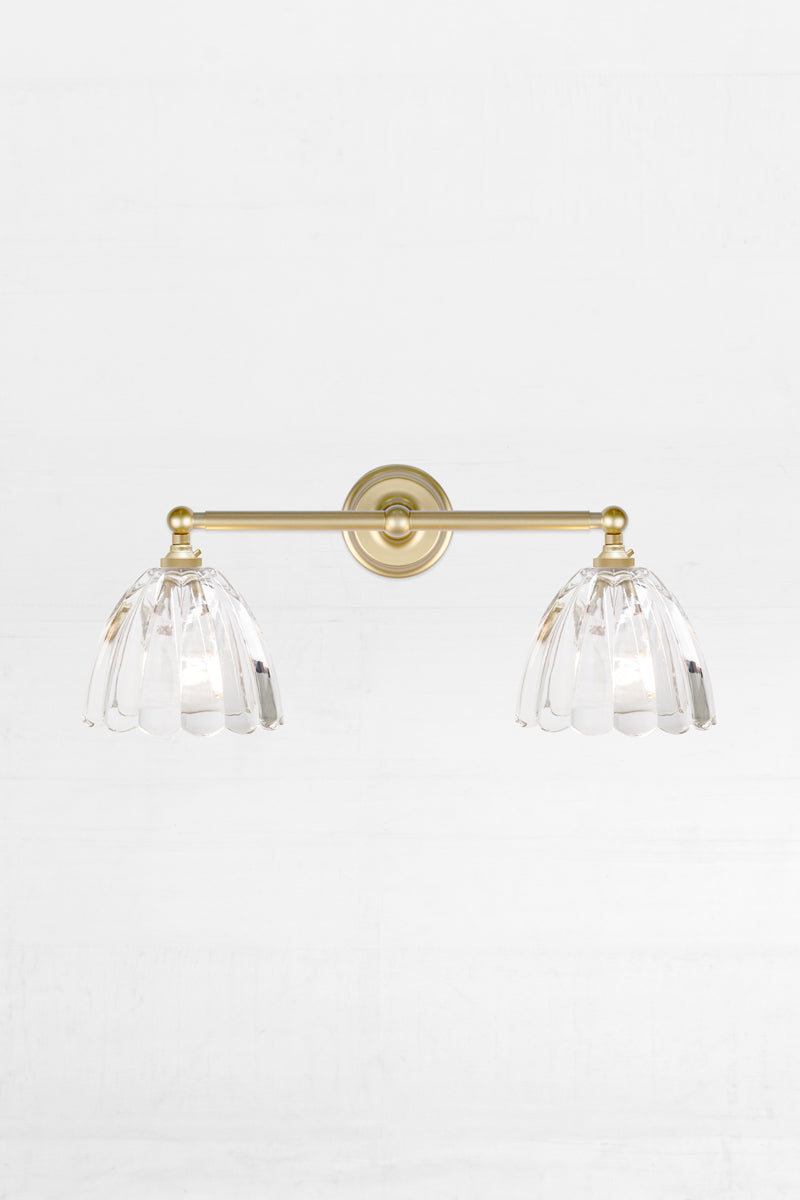 Front view of the gold/brass double swivel wall sconce fixture with the two clear scalloped edge glass shades. 