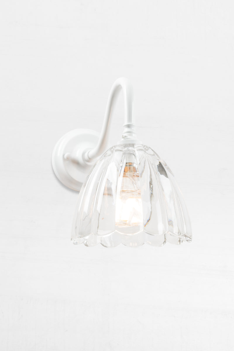 White gooseneck wall sconce with a clear glass shade with a scalloped edge. 