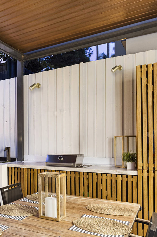 Outdoor kitchen area with brass adjustable wall light on light timber panelling in a courtyard. 